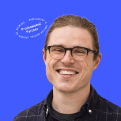 Smiling man with glasses and tied-back hair wearing a dark button-up shirt against a solid blue background with white circular text on the upper left that reads "Professional Partner."
